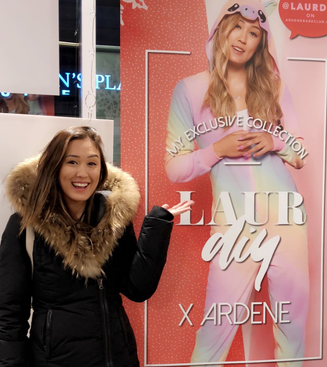 Lifestyle woman standing next to big poster of herself in unicorn onesie